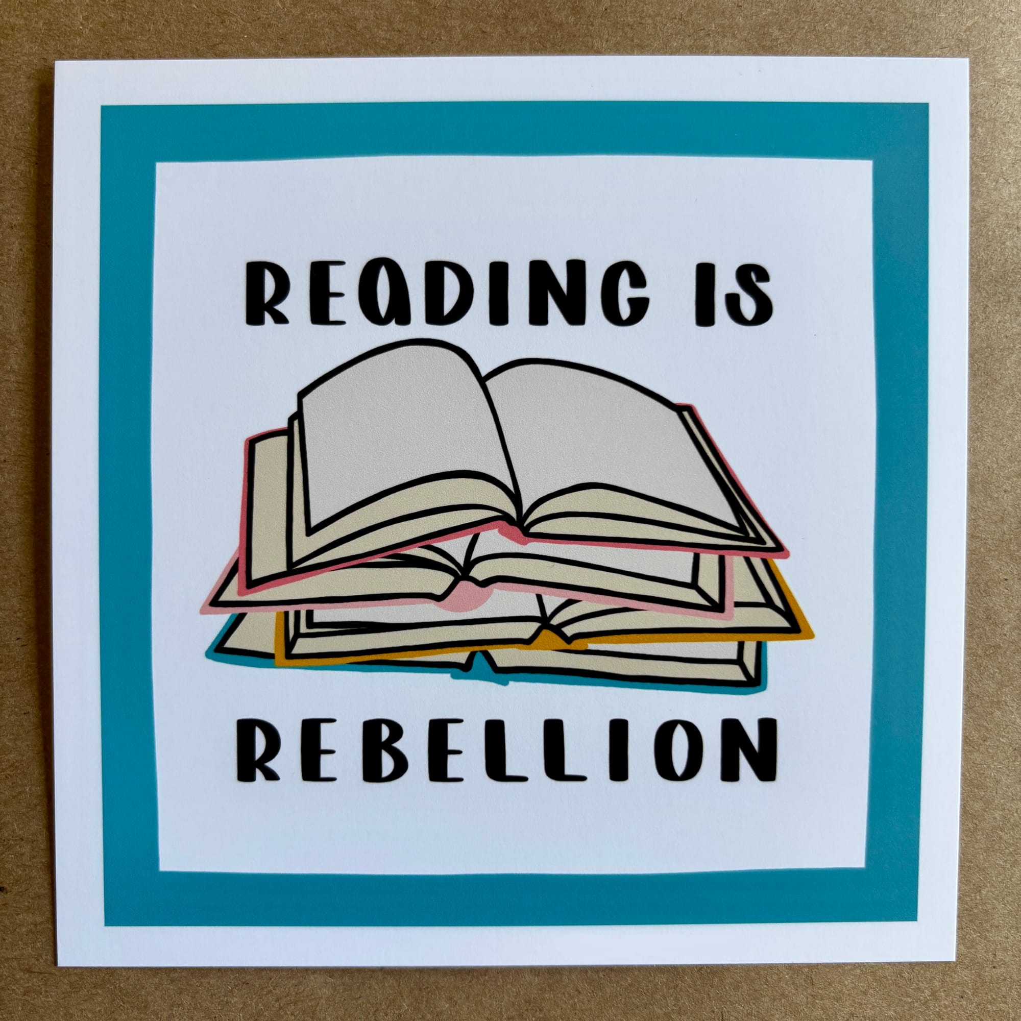 original art by AnneArchy depicting a stack of open books with hand lettering of the words "reading is rebellion"