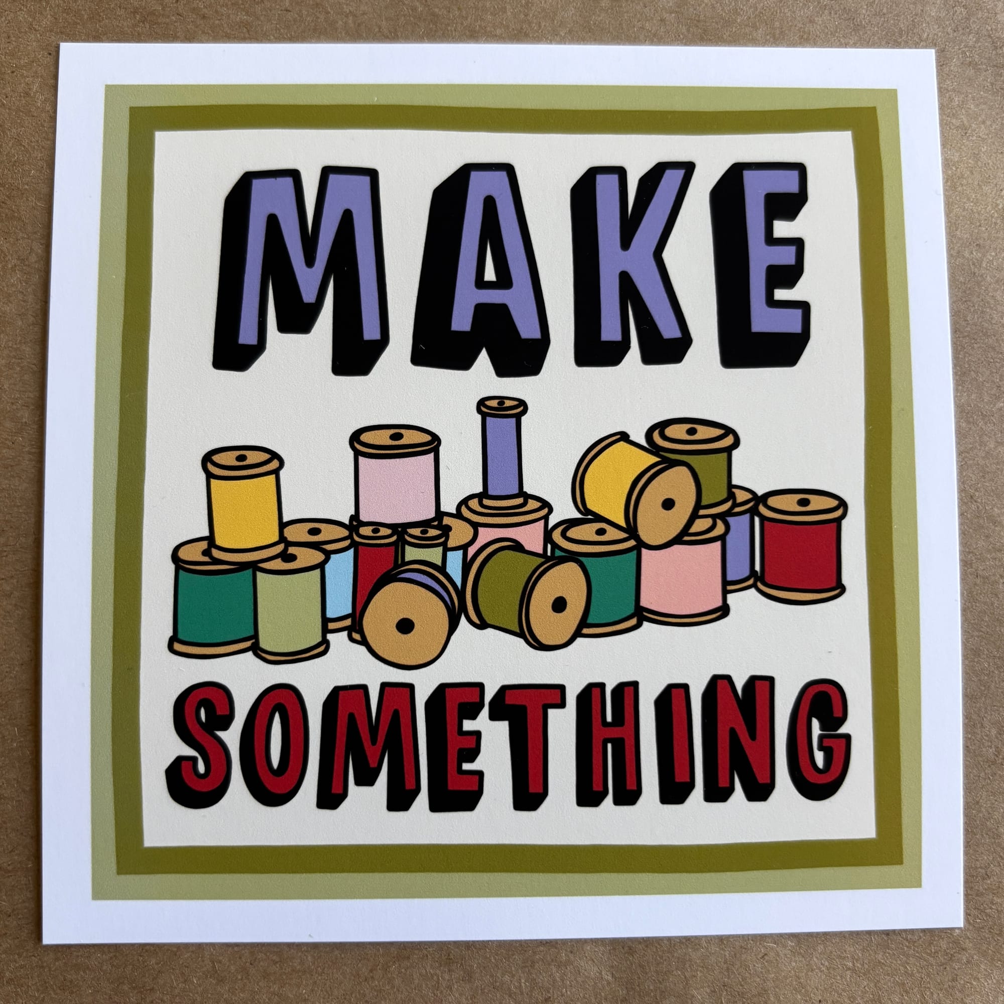 original art by AnneArchy depicting many spools of thread in various colors with hand lettering of the words "make something." 