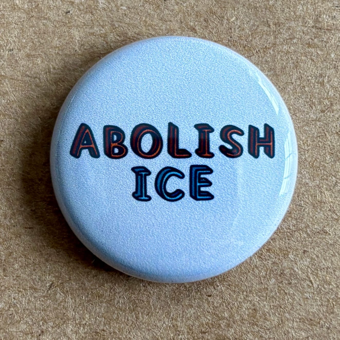 a pin back button with hand lettering by AnneArchy of the words "abolish ICE"